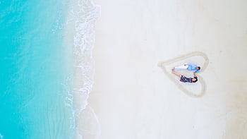 Aerial view of a couple lying on a beach in the Maldives, framed in a heart shape in the sand. HD wallpaper