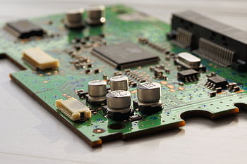 Detailed view of a green circuit board featuring capacitors and microchips. HD wallpaper