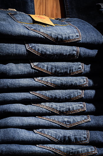Neatly stacked blue jeans with visible price tag in retail setting. HD phone wallpaper