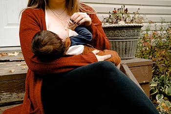 Intimate moment of a mother breastfeeding her child on a porch, symbolizing warmth and care. HD wallpaper