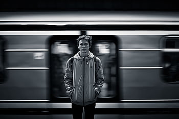 A young man stands still as a subway train moves past in a blurred motion. HD wallpaper