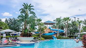 Vibrant tropical resort scene featuring a pool, waterslide, and lush palm trees, ideal for summer vacations. HD wallpaper
