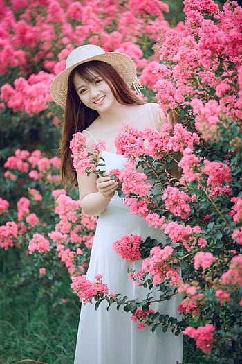 A woman in a white dress and straw hat smiles in a garden surrounded by pink blossoms. HD phone wallpaper