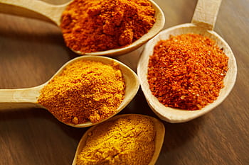 Close-up of vibrant spices like turmeric and chili powder in wooden spoons. HD wallpaper