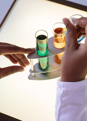 Hands conducting an experiment with colorful test tubes in a lab setting. HD phone wallpaper