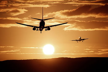 Silhouetted airplanes landing against a dramatic sunset sky, capturing the essence of flight. HD wallpaper