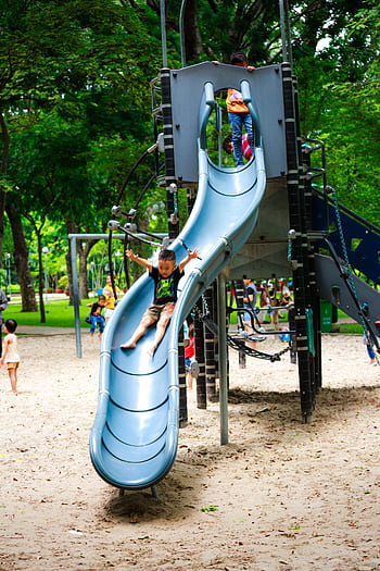 Children having fun on a slide in a lively park playground on a bright day. HD phone wallpaper