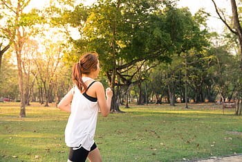 A woman jogging through a forest park in the early morning sunshine, enjoying a healthy lifestyle. HD wallpaper