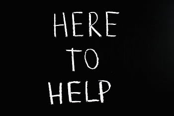 White text 'Here to Help' on a minimalist black chalkboard background, conveying encouragement and support. HD wallpaper