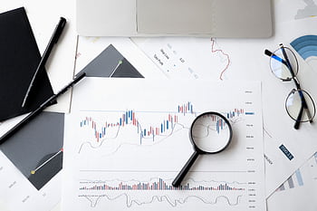 Flat lay of stock market analysis documents with magnifying glass, pens, and glasses. HD wallpaper