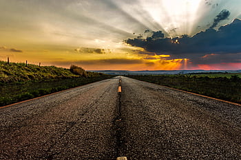 Dramatic sunset over an empty rural highway with vibrant skies and sunrays. HD wallpaper
