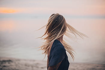 Blonde woman enjoying a serene sunset by the beach, capturing the essence of tranquility. HD wallpaper