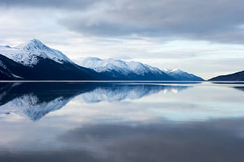 Beautiful snow-capped mountains reflected in a calm lake under a cloudy sky, evoking a tranquil winter landscape. HD wallpaper