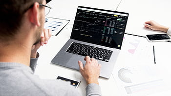Business professional analyzing stock market data on a laptop for investment insights. HD wallpaper