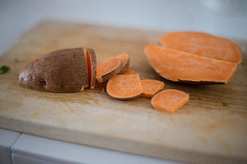 Close-up of sliced sweet potato on a wooden cutting board, perfect for cooking inspiration. HD wallpaper