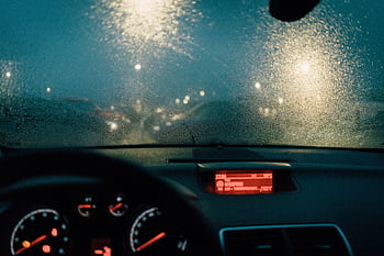 View from car interior with raindrops on windshield and blurred lights at night. HD wallpaper