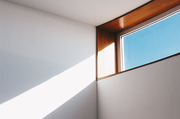 A minimalist interior showcasing sunlight streaming through a modern glass window against a blue sky. HD wallpaper