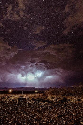 Stunning night capturing a thunderstorm under a starry sky, showcasing dramatic lightning and cloud formations over a desert landscape. HD phone wallpaper