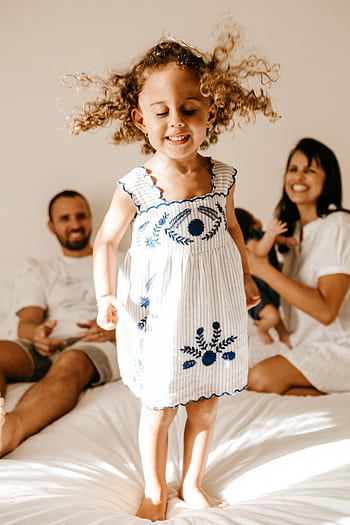 A cheerful family enjoying a playful moment indoors, featuring a delighted child jumping on the bed. HD phone wallpaper
