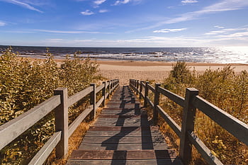 A wooden stairway leads to a tranquil sandy beach with views of the endless ocean under a clear blue sky. HD wallpaper