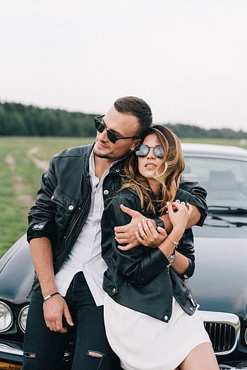 Charming couple in black leather jackets embracing by a car in the countryside. HD phone wallpaper