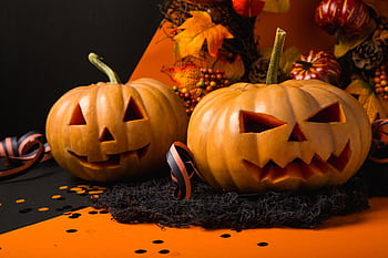 Two carved pumpkins with spooky faces set against an autumnal background for Halloween. HD wallpaper
