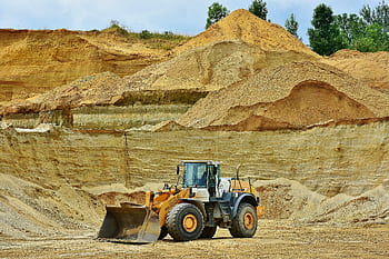 An excavator working in an open pit mine surrounded by sandy terrain and clear sky. HD wallpaper
