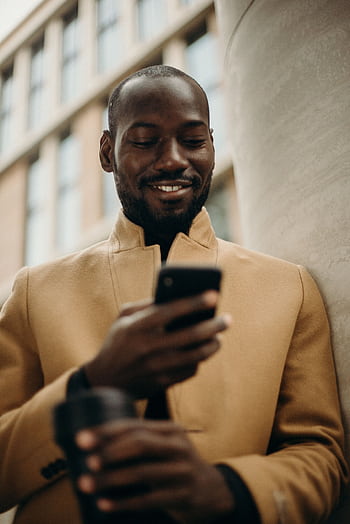 A cheerful man in a stylish coat using his smart and holding coffee outside. HD phone wallpaper