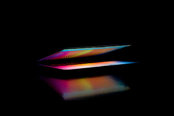 A colorful, partially open laptop screen reflects light in a dark setting. HD wallpaper