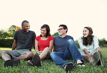 A group of young adults smiling while sitting on grass in a sunny park, enjoying friendship and leisure. HD wallpaper