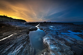 Dramatic sunset over a rocky coastline, capturing tranquil ocean scenery. HD wallpaper