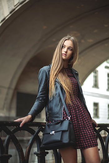 Stylish woman poses with a black leather jacket and dress in a city street, embodying modern fashion. HD phone wallpaper