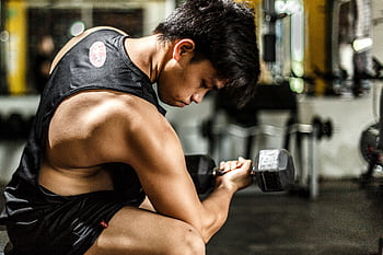 Young man intensely lifting a dumbbell in a gym, highlighting strength and focus. HD wallpaper