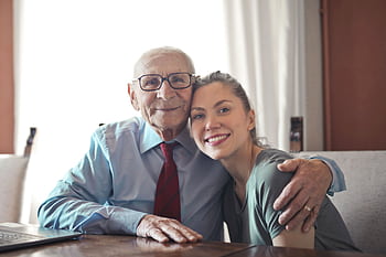 A joyful elderly man and young woman sharing an affectionate embrace indoors. HD wallpaper