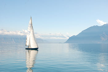 Sailing boat glides peacefully on a misty lake surrounded by mountains, under clear daylight. HD wallpaper