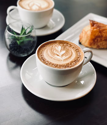 Delicate latte art in a café setting with a pastry and plant on a polished table. HD phone wallpaper