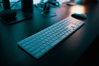 A modern wireless keyboard placed on a sleek desk, illuminated by ambient lighting in a tech-savvy office setting. HD wallpaper