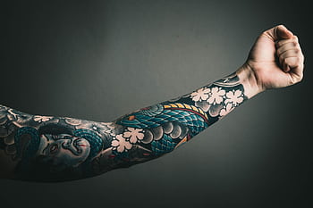 A close-up of a tattooed arm with a colorful sleeve design, featuring floral and artistic elements. HD wallpaper