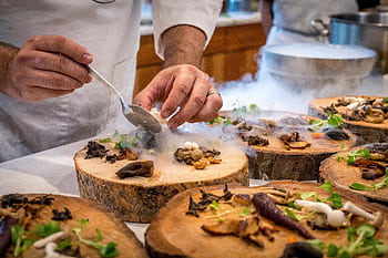 A chef artfully plating a gourmet dish with mushrooms and greens on wood slices. HD wallpaper