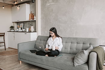 Woman in a modern living room working on a laptop and enjoying a coffee. HD wallpaper