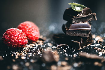 Artistic close-up of dark chocolate pieces with fresh raspberries, perfect for dessert visuals. HD wallpaper