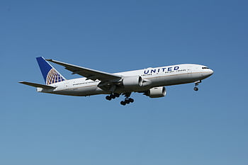 A United airliner flying against a clear blue sky, showcasing air travel. HD wallpaper