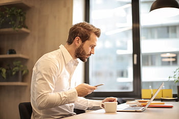 Focused businessman working on laptop while checking smart in modern office. HD wallpaper