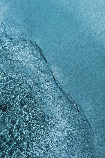 Serene aerial view of a blue ocean meeting a sandy shoreline, showcasing nature's beauty. HD phone wallpaper