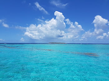 Scenic view of bright turquoise sea with fluffy clouds on a tranquil day. HD wallpaper