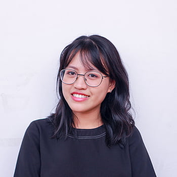 Portrait of a young woman with glasses and black hair smiling against a plain background. HD phone wallpaper