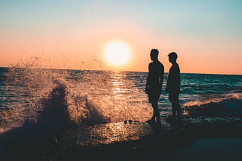 Two people silhouetted against a vibrant sunset at Laguna Beach, CA. HD wallpaper
