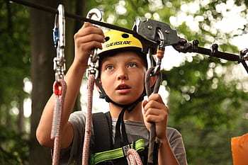 A young boy enjoying a rope climbing activity outdoors, wearing a helmet and using safety gear. HD wallpaper