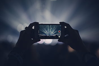 Hands holding smart to record concert with vibrant stage lights. HD wallpaper