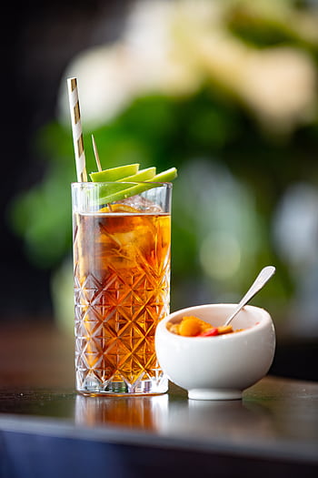 Refreshing iced tea with green apple garnish beside a bowl of colorful fruits. HD phone wallpaper